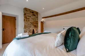 Ein Schlafzimmer mit Kamin aus Stein, Holzbalken, einem Bett mit weißen Leinentüchern und einer Tür.
