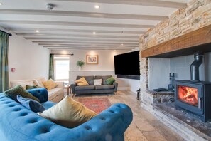 Ein Wohnzimmer mit Kamin aus Stein, einem blauen Sofa, einem grauen Sofa und einem an der Wand montierten Flachbildfernseher.