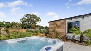 A hot tub in a backyard with a wooden fence, a lawn, and a small building with a window. - 4 Bed in Berrow (oc-h32250) (Berrow)