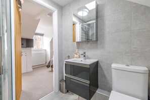 A modern bathroom with a grey tiled wall, a white sink, a mirror, and a toilet. - 3 Bed in Old Hunstanton (oc-2104) (Hunstanton)