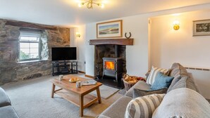 A cozy living room with a stone wall, a fireplace, a television, and a comfortable sofa. - 1 Bed in Llanfair (oc-b32109) (Llanfair)
