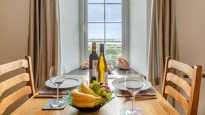 A dining table with two chairs, a bottle of wine, a bowl of fruit, and a view of the countryside through a window. - 1 Bed in Llanfair (oc-b32109) (Llanfair)