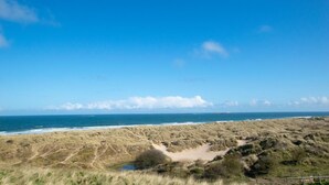 Ett kustlandskap med sanddyner, en strand och en klar himmel.