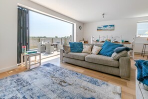 A living room with a sofa, a coffee table, a rug, and a dining area with chairs and a table. - 3 Bed in Woolacombe (oc-c32222) (Woolacombe)