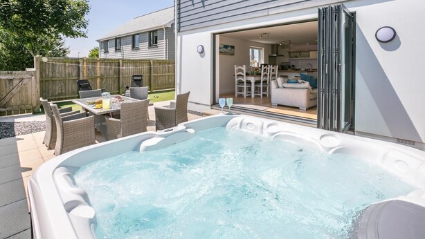 A hot tub in a backyard with wicker furniture and a dining area visible through an open door. - 3 Bed in Woolacombe (oc-c32222) (Woolacombe)
