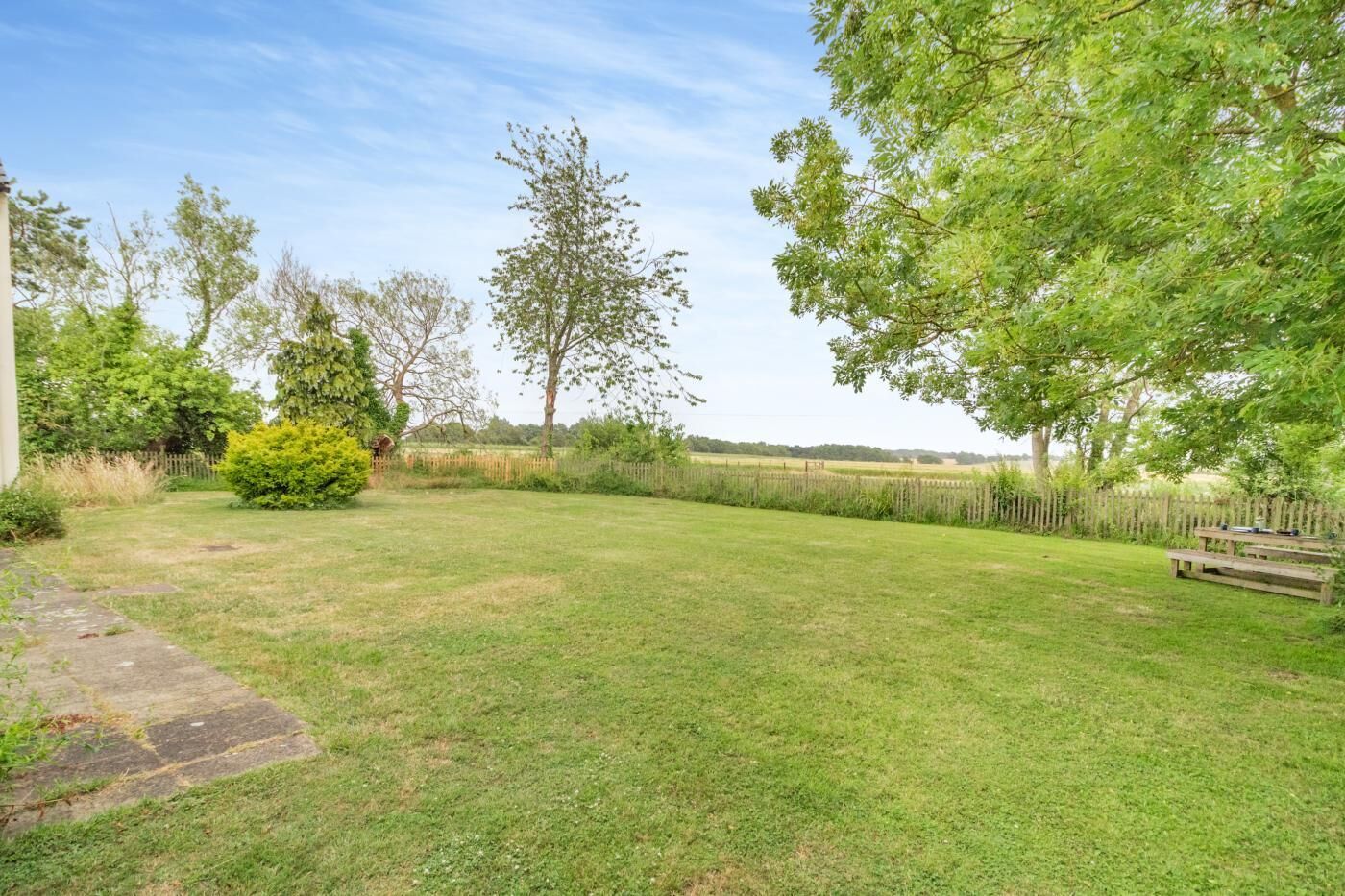 A grassy backyard with a wooden bench, trees, and a fence.
