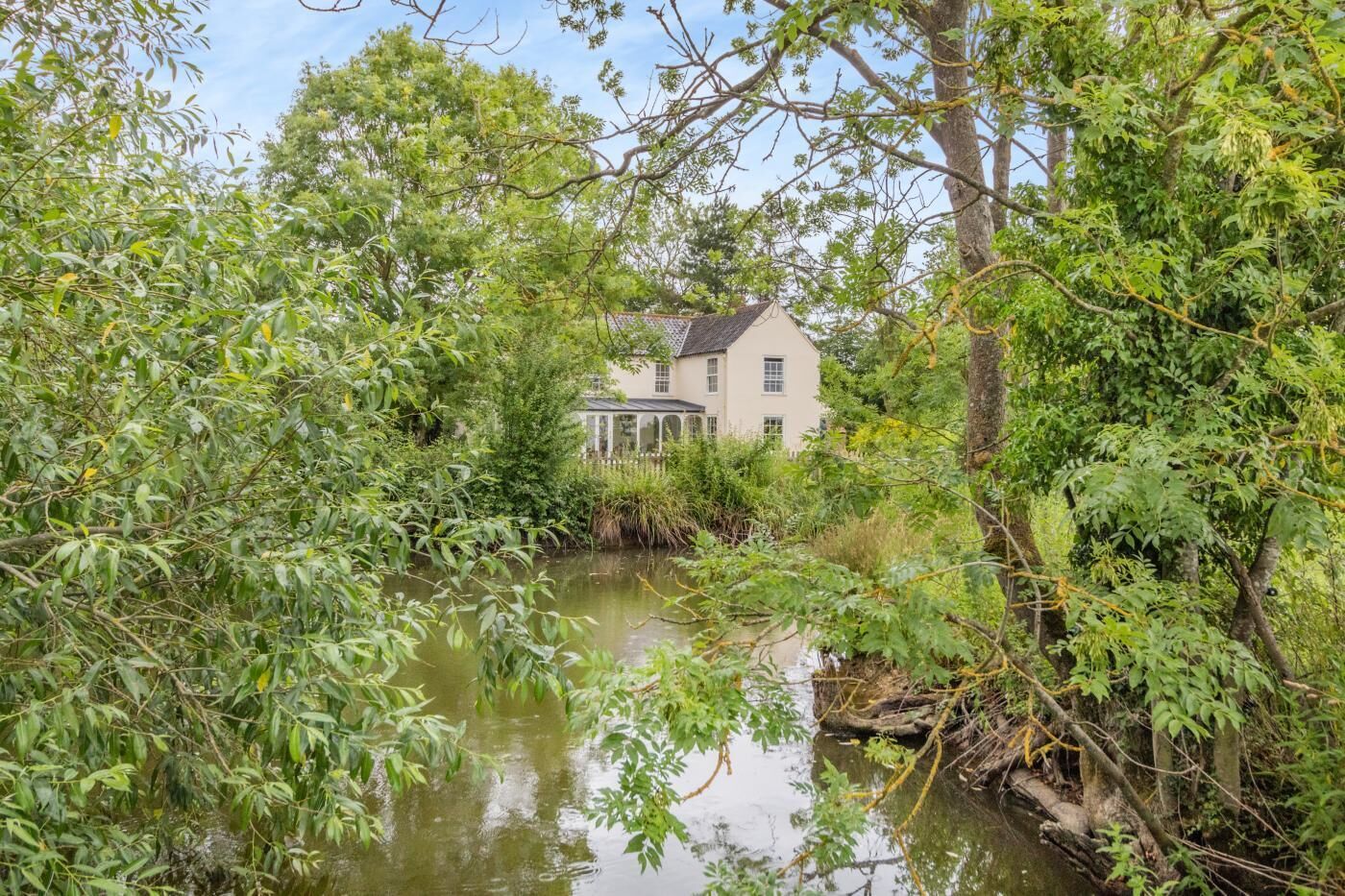 A house surrounded by dense foliage and a calm water body.