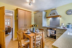 A kitchen with wooden cabinets, a dining table with chairs, a stove, and a clock on the wall. - 2 Bed in Rowrah (oc-s32232) (Arlecdon)