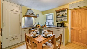 Una cocina compacta con una mesa de comedor para cuatro personas, un microondas, un fregadero y un reloj en la pared.