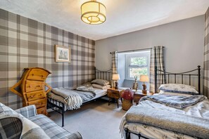 Une chambre avec deux lits, une commode en bois, une fenêtre avec des rideaux et un luminaire suspendu.