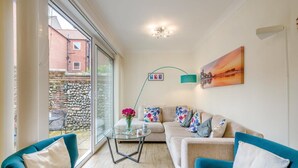 A modern living room with a sofa, two armchairs, a glass coffee table, and a view of a stone wall and building outside. - 3 Bed in Cromer (oc-2103) (Cromer)