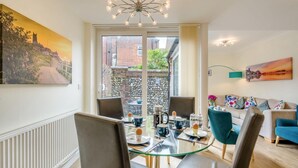 A modern living room with a glass dining table, comfortable seating, a sofa, and a view of a cityscape through large windows. - 3 Bed in Cromer (oc-2103) (Cromer)
