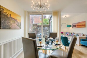 A modern living room with a glass dining table, comfortable seating, a sofa, and a view of a cityscape through large windows. - 3 Bed in Cromer (oc-2103) (Cromer)