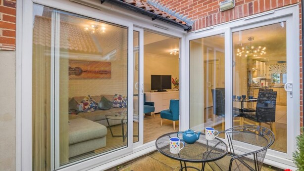 A modern home with a patio area featuring a round metal table, two chairs, and a blue teapot. - 3 Bed in Cromer (oc-2103) (Cromer)