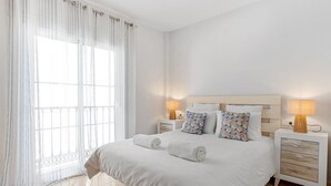 Hotelkamer met een groot bed, twee nachtkastjes, een raam met lichte gordijnen en uitzicht op de stad.