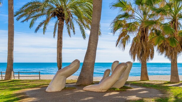Een strand met palmbomen en een beeld van zittende figuren.