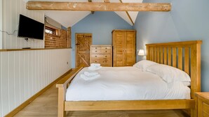 Een slaapkamer met een houten bed, witte lakens, een aan de muur bevestigde televisie en een bakstenen muur.