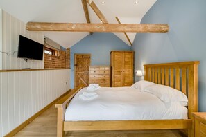 Ein Schlafzimmer mit einem hölzernen Bett, weißen Bettwäsche, einem an der Wand montierten Fernseher und einer Ziegelwand.