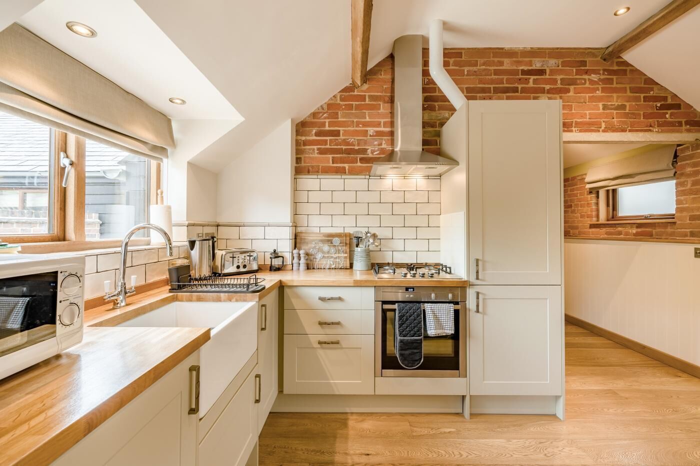 A kitchen with a brick wall, white cabinets, a wooden countertop, and a window.