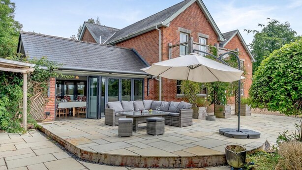 Une terrasse avec mobilier d’extérieur, un espace repas couvert et une maison en briques avec un toit en pente.