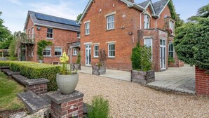 Une maison en briques avec un jardin, un grand bac à fleurs et une allée gravillonnée.