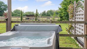 A hot tub with a wooden deck and a view of a fenced outdoor area with trees and a building in the background. - 1 Bed in Blashford (oc-d32251) (Ringwood)