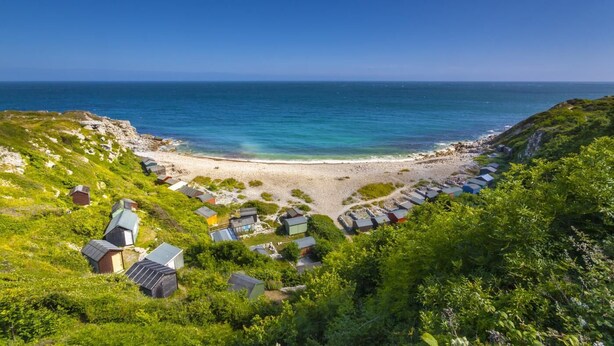Zona costera con una playa, varias cabañas pequeñas y vegetación exuberante.