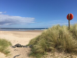 A beach with a red circular sign, sandy terrain, and grass. - 4 Bed in Amble (oc-gd1880) (Amble)