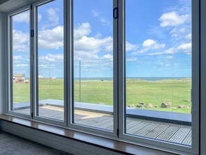 Een kamer met grote ramen, met uitzicht op een grasveld en verderop een stuk water.