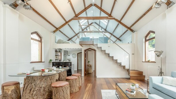 Ein großzügiger Wohnbereich mit einem großen Esstisch aus Holz, einer Treppe zu einer oberen Ebene und einer modernen Küche im Hintergrund.