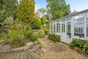 A conservatory with a wooden deck, surrounded by diverse garden plants and trees. - 5 Bed in Battle (oc-l32238) (Battle)