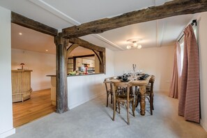 A dining area with a wooden table set for six, surrounded by chairs, and a rustic wooden beam ceiling. - 5 Bed in Battle (oc-l32238) (Battle)