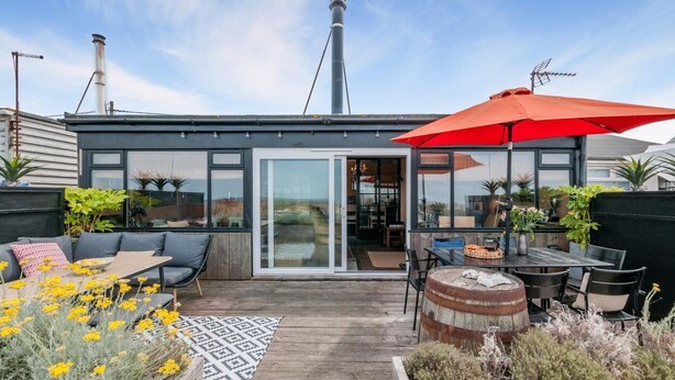 A modern house with a patio area featuring a wooden deck, outdoor furniture, and a red umbrella.