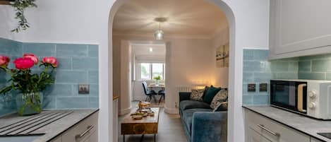 A modern kitchen with a central island, a dining area with a sofa, and a view through an archway.