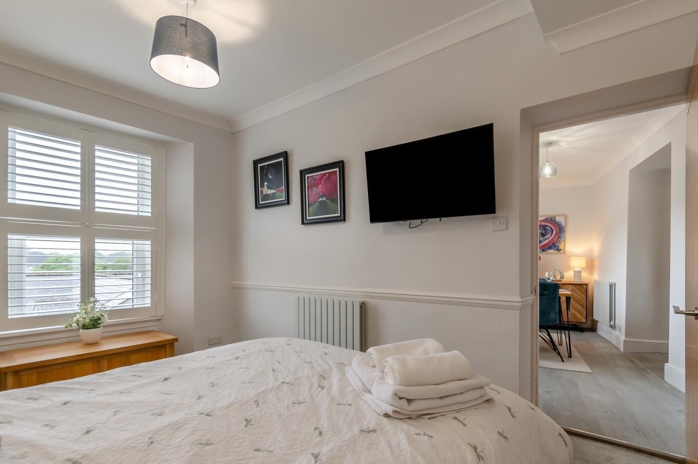 A bedroom with a bed, a flat-screen TV, and a window with blinds.
