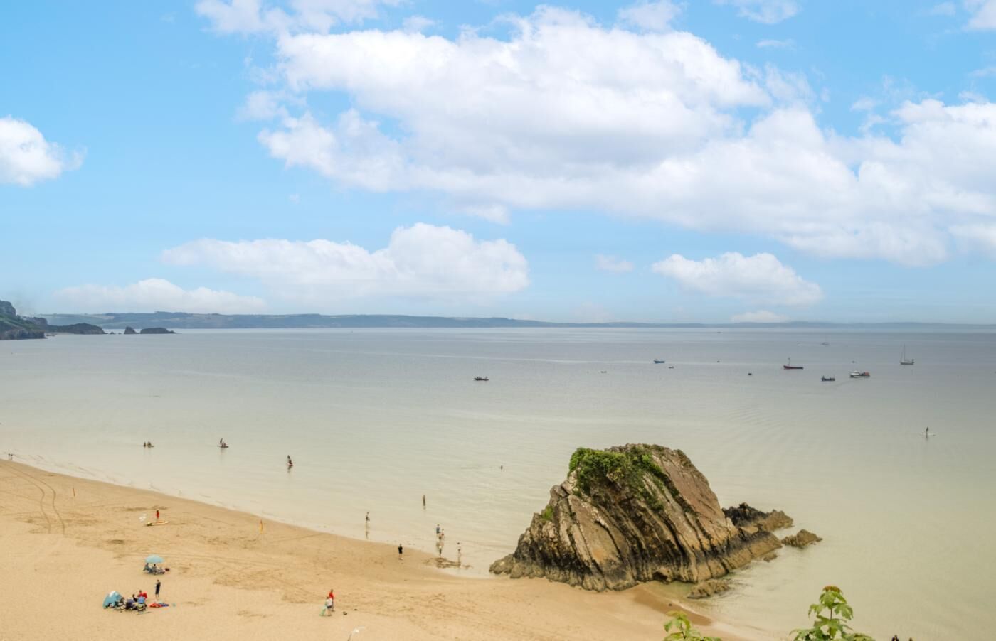 A beach with a rocky outcrop, calm sea, and distant land.