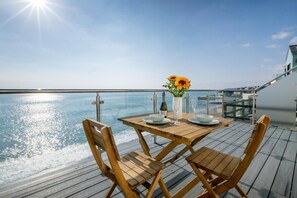 Une terrasse en bois avec une table dressée pour deux personnes, donnant sur une mer calme.