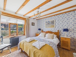 A bedroom with a bed, a window with curtains, a radiator, a wooden chair, a nightstand, and a lamp. - 2 Bed in Whitby (oc-w014) (Whitby)