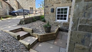 A stone building with a small garden area, a wooden bench, and a paved walkway.