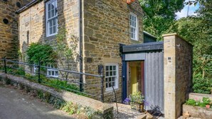 A stone building with a wooden door, a metal railing, and a small garden area.