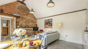 Un comedor con pared de ladrillo, una mesa de madera dispuesta con platos, vasos y un ramo de flores blancas.