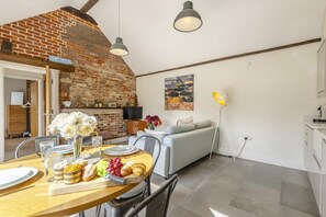 Un coin repas avec un mur en briques, une table en bois dressée avec des assiettes, des verres et un bouquet de fleurs blanches.