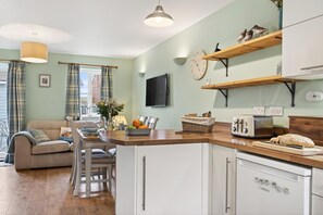 A modern kitchen with a Bosch dishwasher, wooden shelves, a clock, and a dining area with a sofa and table. - 2 Bed in Whitby (oc-w502) (Whitby)