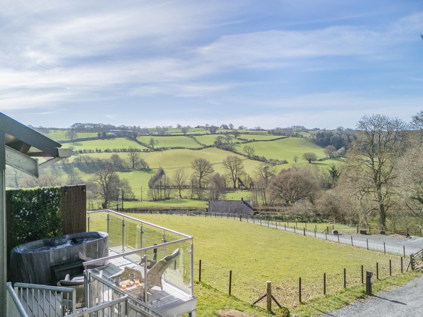 Un bain à remous sur un balcon donnant sur un paysage rural, avec des collines ondoyantes et un champ clôturé.