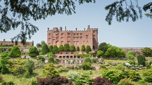Un vaste château historique, doté de nombreuses tours et d’un jardin bien entretenu à l’avant.