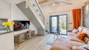 Un salon moderne avec un escalier, un téléviseur, un canapé et un coin repas.