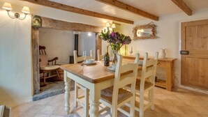 Un comedor con una mesa y sillas de madera, un jarrón con flores y una lámpara fijada a la pared.