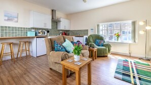 Een ruimtelijk ingerichte leefruimte met kitchenette, een bank, een stoel en een kleine tafel.