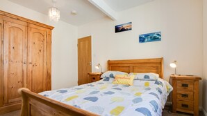 Een slaapkamer met een houten bed, twee nachtkastjes, een houten garderobe en twee aan de muur bevestigde schilderijen.