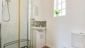 Een badkamer met een douche, wastafel, toilet en een raam met een plant.